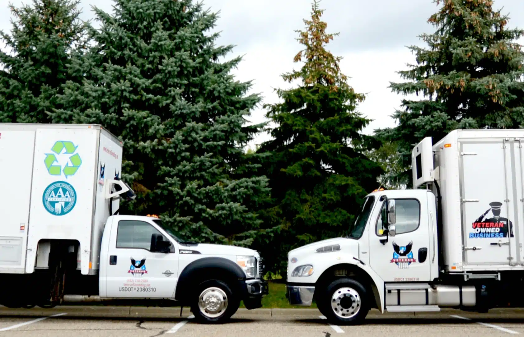 Two Veteran Shredding trucks parked facing each other in a lot with trees in the background.